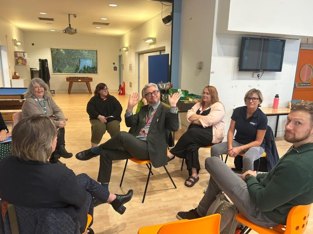 Attendees sitting in a circle at the Bridgwater Neighbourhood meeting. A man in the centre of the circle is smiling and waving his hands.