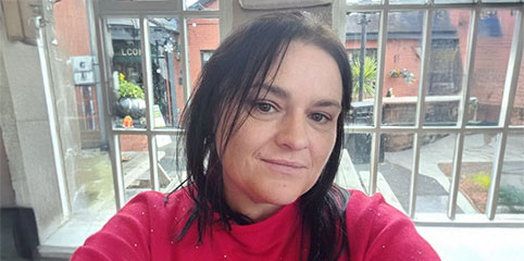 Anne is a middle aged woman with shoulder length black hair wearing a red jumper